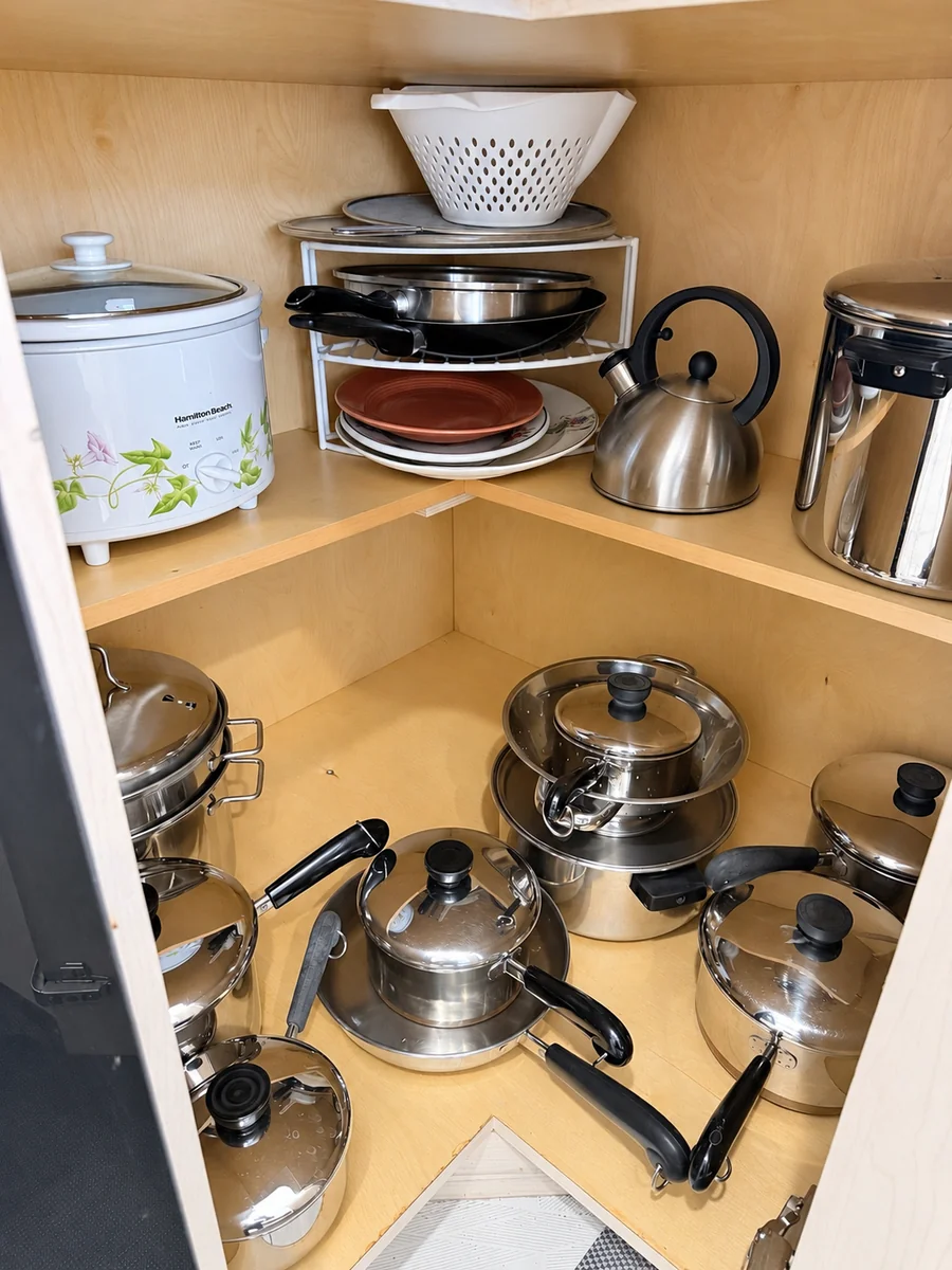 Open cabinet holding pots, pans, lids, plates, a kettle, and a colander