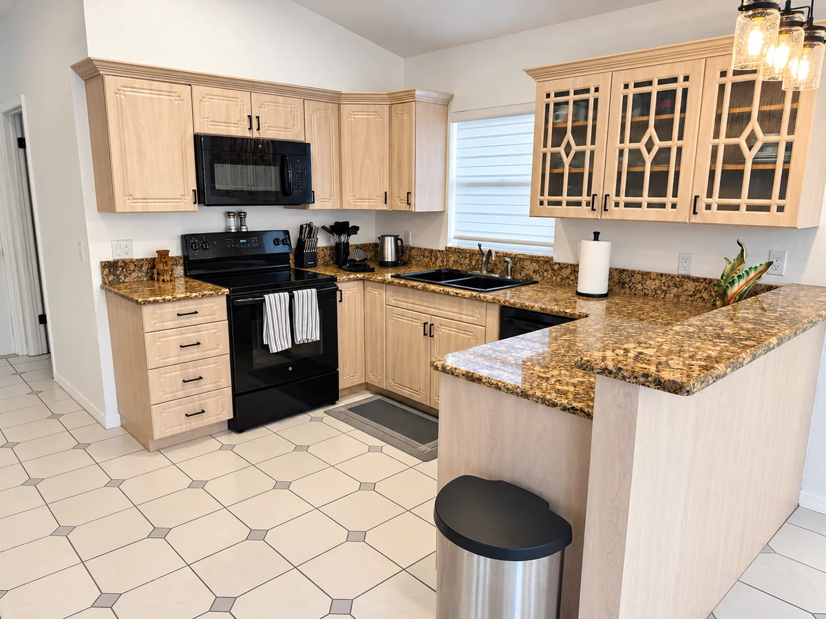 Kitchen with light wood cabinets, granite counters, stove, microwave, and sink